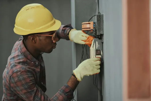 Electrician cu cască lucrând la un tablou electric